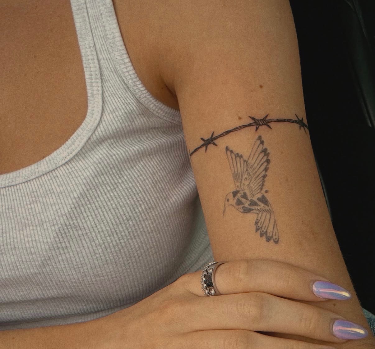 Fine line hummingbird and barbed wire tattoo on an arm